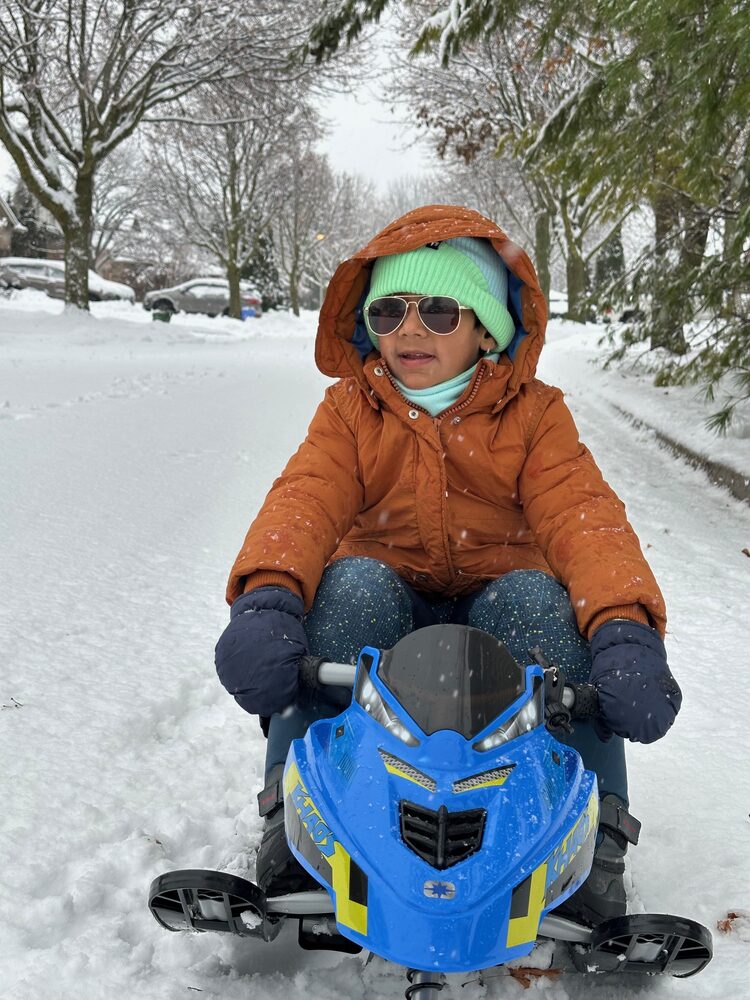 Kedaar bundled up on a kid-sized snowmobile in the snow
